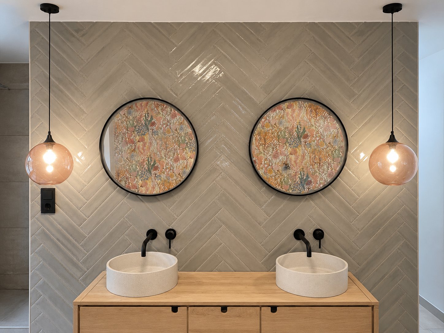 Doppelwaschtisch mit zwei runden Aufsatzwaschbecken vor einer Wand mit glaenzenden Fischgraetfliesen, schwarze Unterputz-Wandarmaturen und Rauchglas-Pendelleuchten