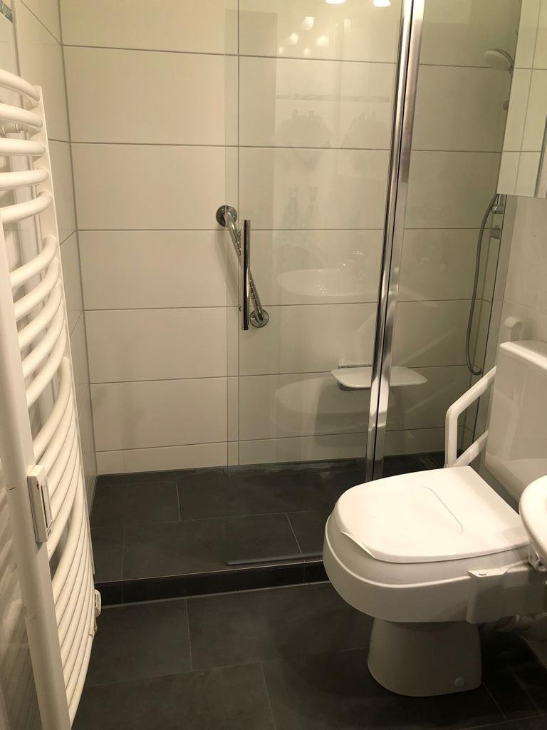Badezimmer nach dem Umbau mit tiefergesetztem, bodengleich gefliestem Duschbereich, Duschrinne und Haltegriff