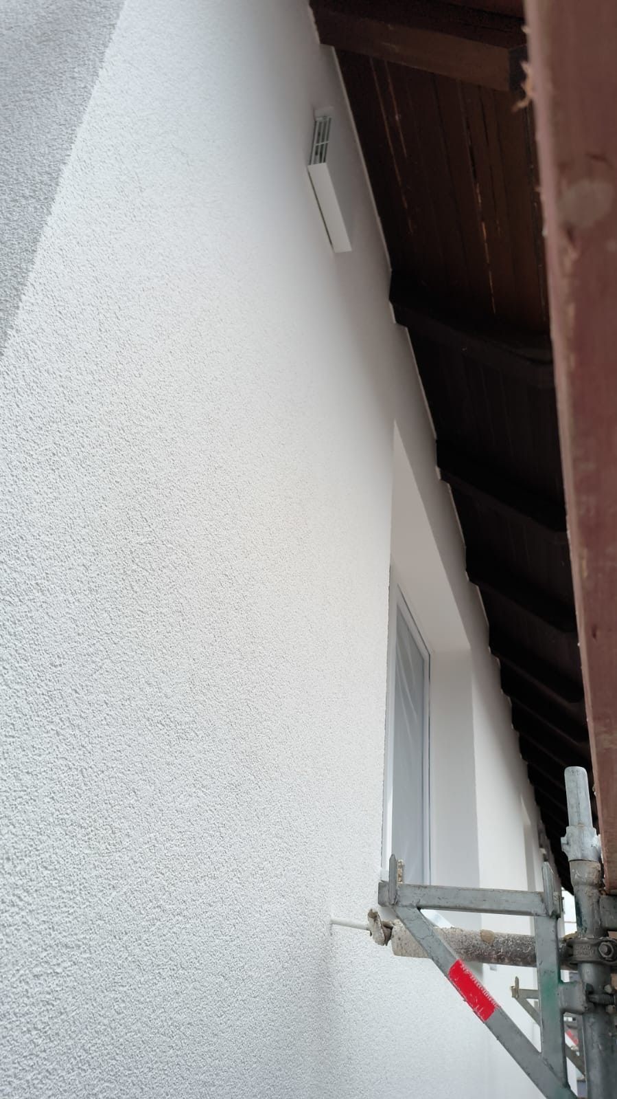 Weiß gestrichene Fassade mit Lüftungsauslass unter dem Dachüberstand