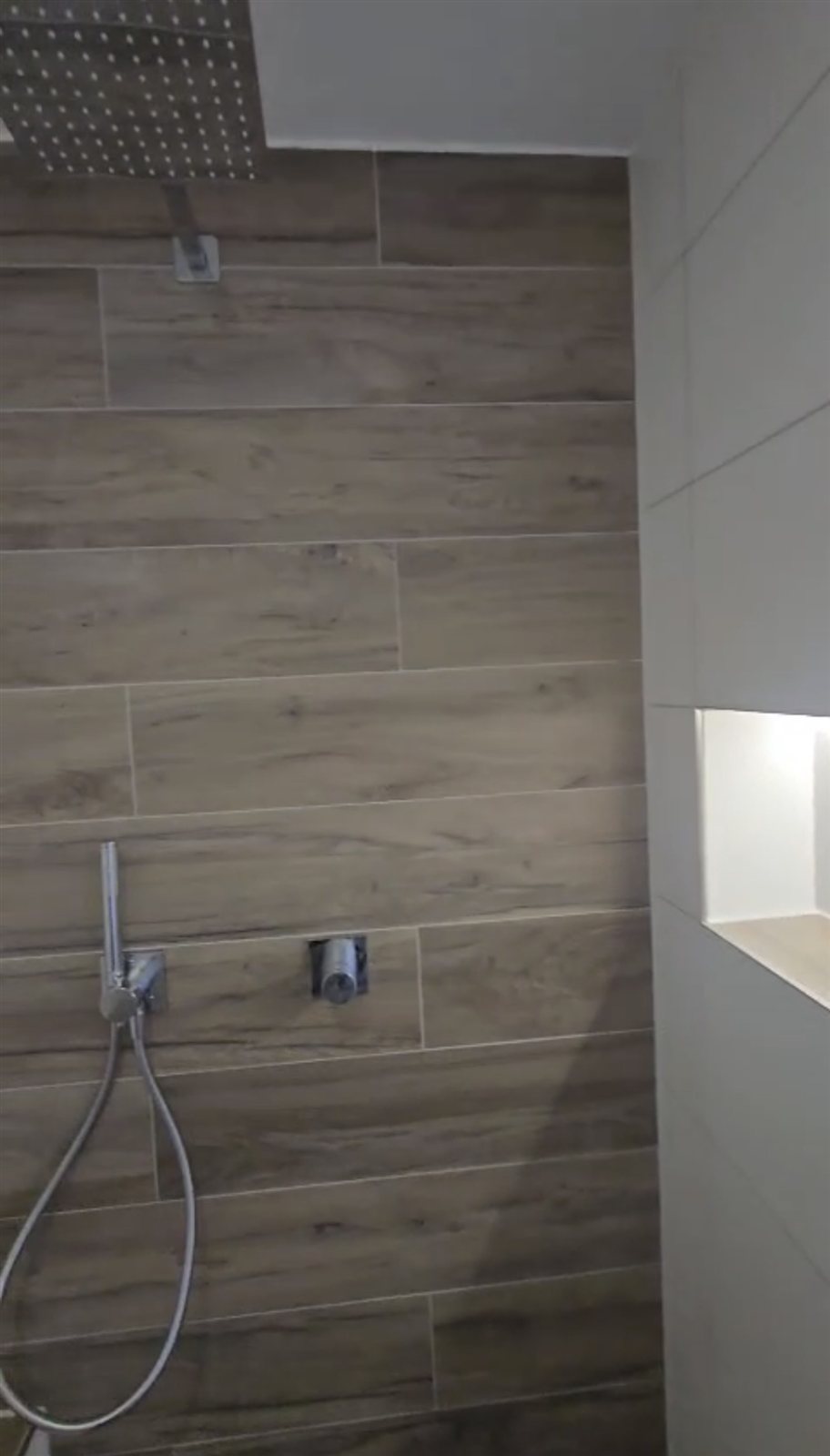 Dusche mit Holzoptik-Fliesen und beleuchtetem Duschfach