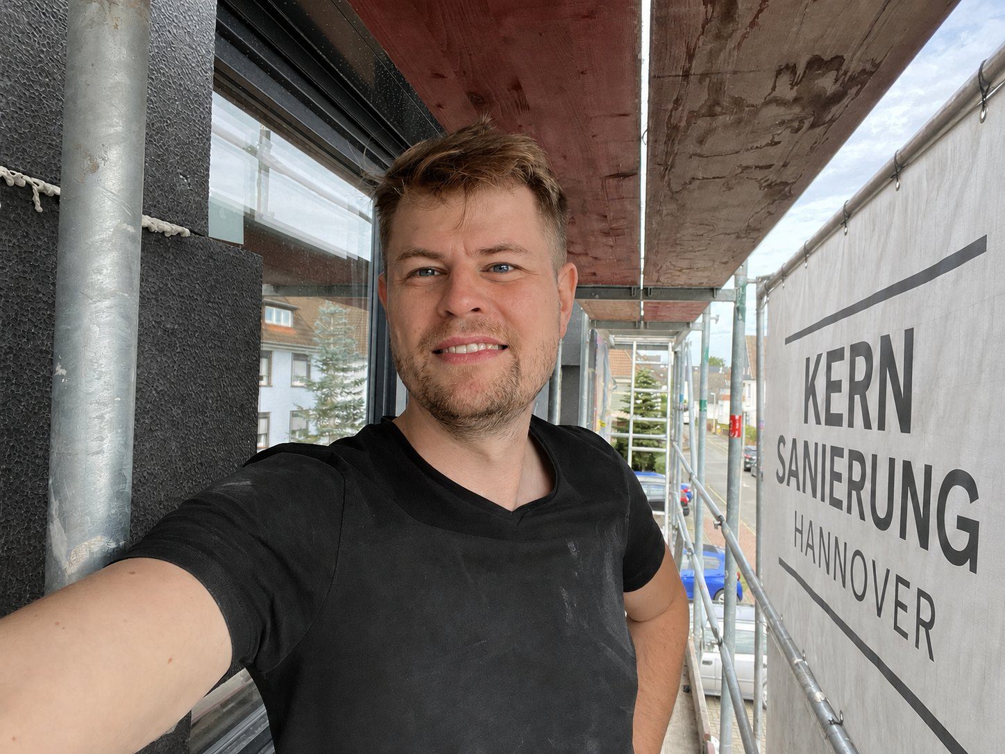 Nils Munzert auf dem Gerüst vor einer gedämmten Fassade, daneben das Gerüstplakat Kernsanierung Hannover